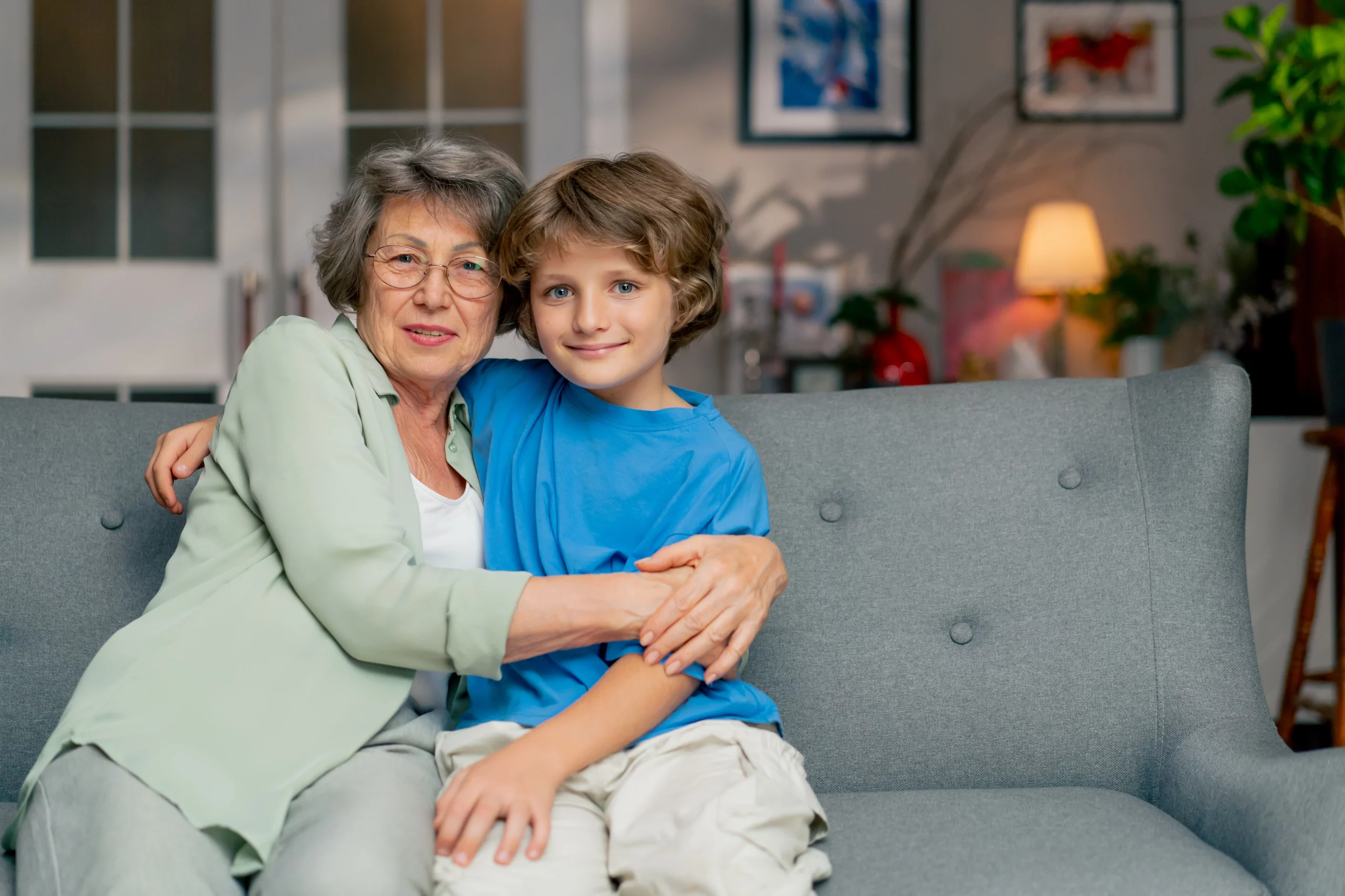Grandmother embraces grandson on gray sofa symbolizing family unity and guardianship care