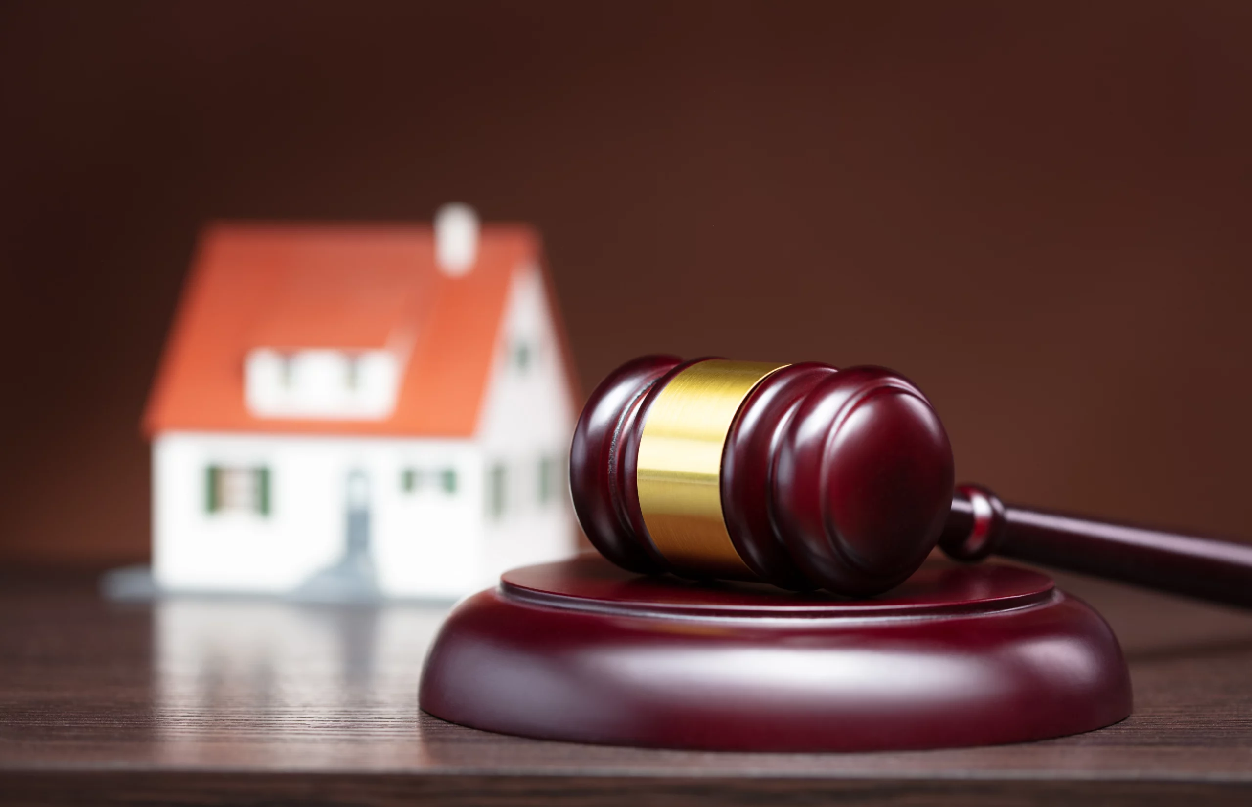 Judge’s gavel on wood surface with model house in background symbolizing real-estate law