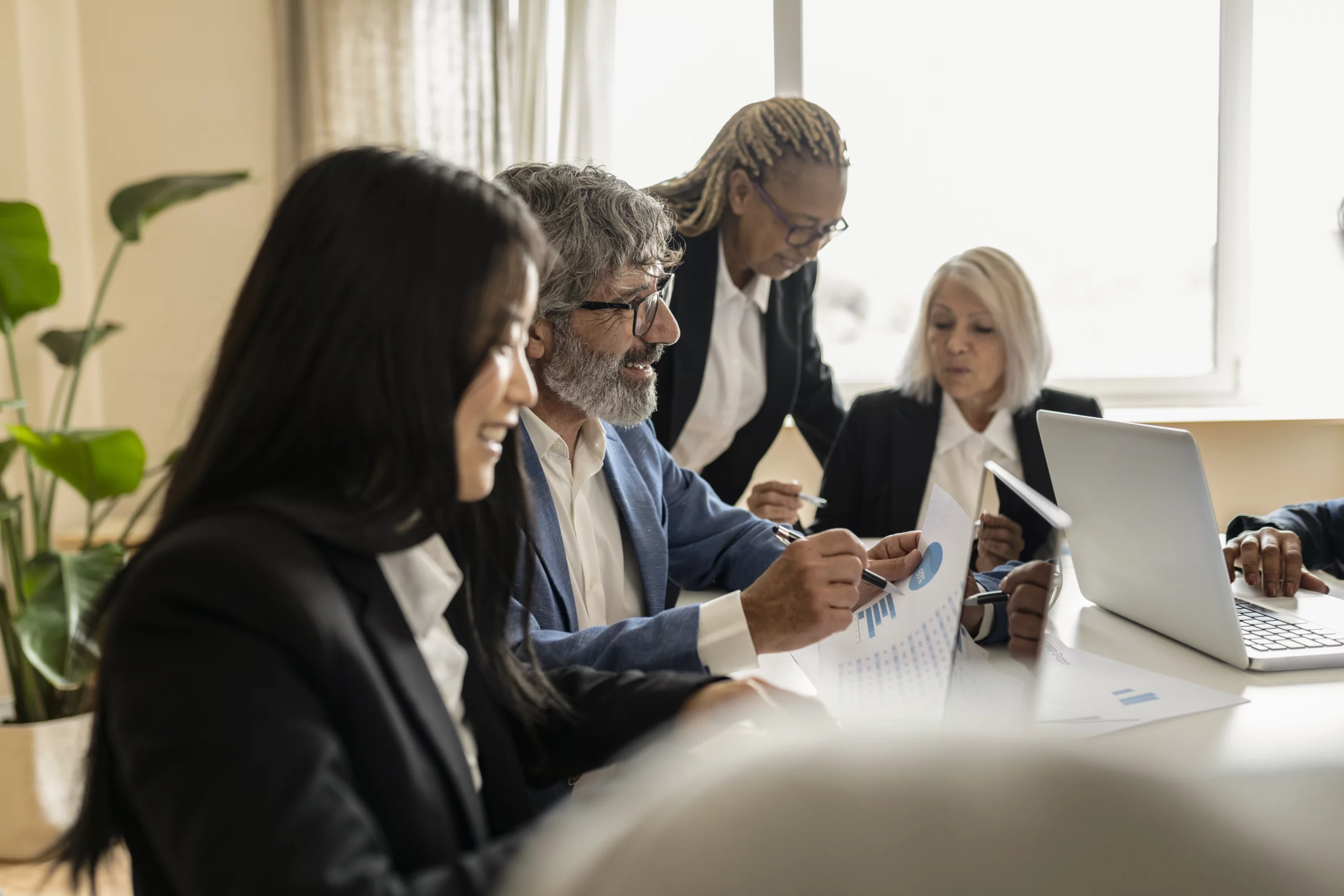 Business professionals in suits reviewing documents and laptop around wooden table — collaboration in business litigation setting in Florida